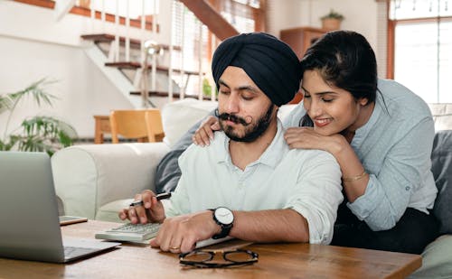 Free Cheerful ethnic couple using calculator while sitting at table Stock Photo