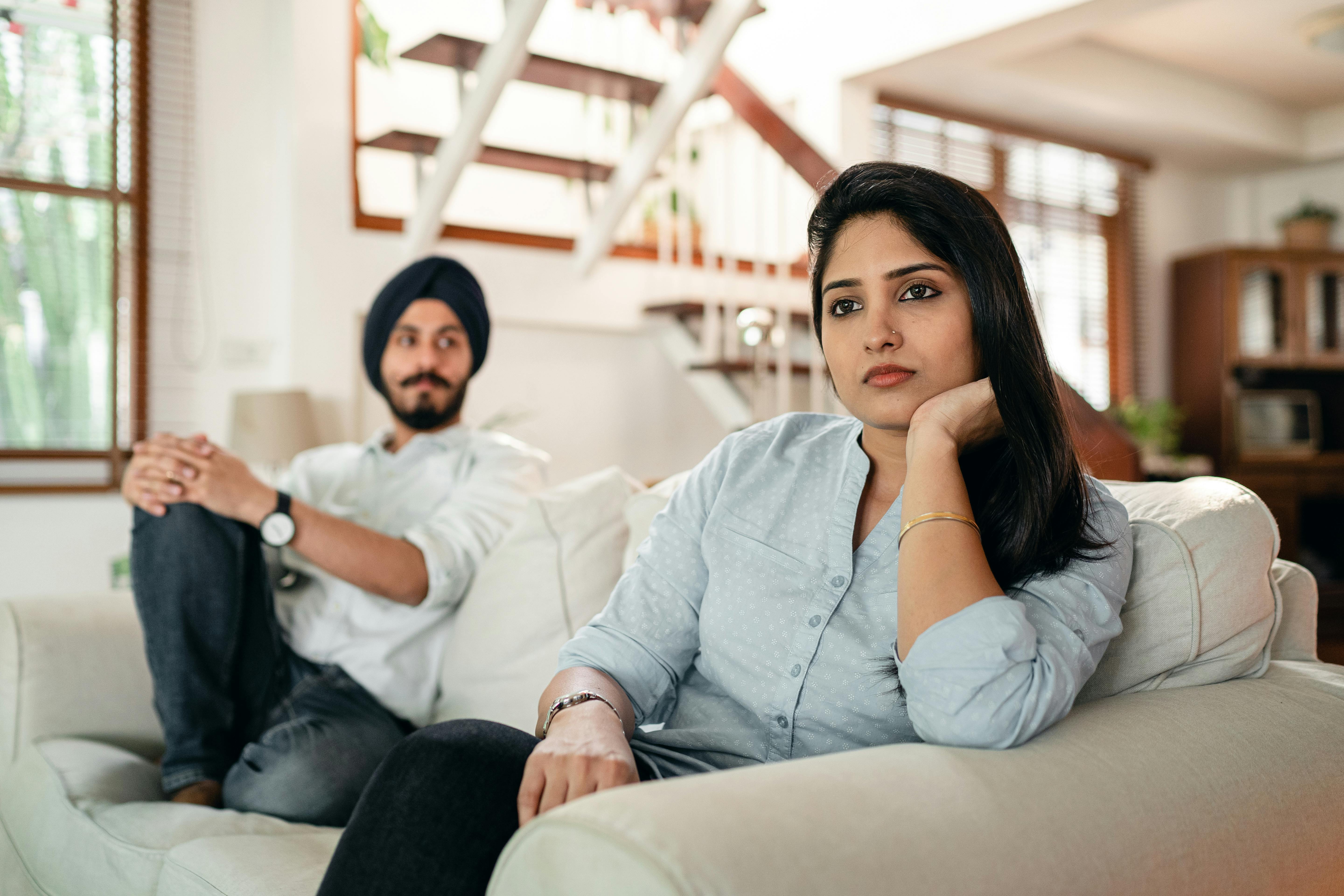 offended young indian female sitting on couch with husband
