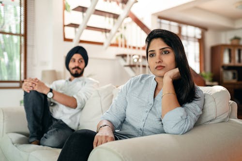 Offended young Indian female sitting on couch with husband