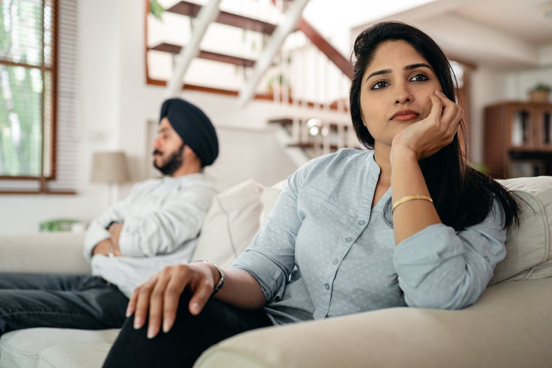 Free Sad young Indian woman avoiding talking to husband while sitting on sofa Stock Photo