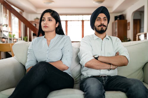 Free Resentful young Indian couple ignoring each other while sitting on couch together with crossed arms Stock Photo