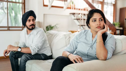 Upset young Indian couple having argument while sitting on couch