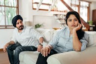 Young ethnic couple sitting on sofa after conflict