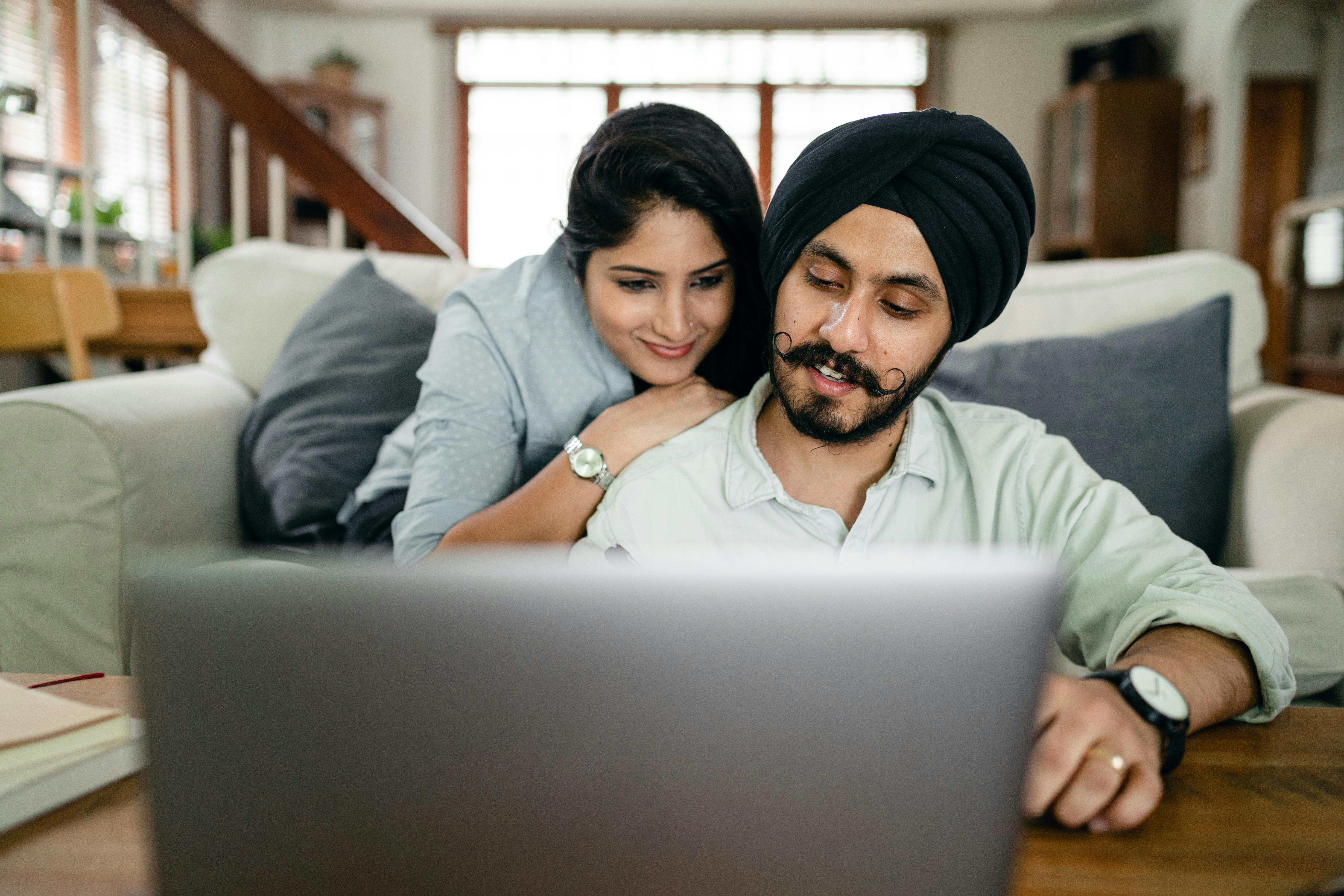 cheerful ethnic couple using laptop and smiling