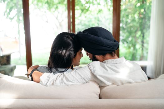 一对年轻的匿名少数族裔夫妇在舒适的客厅沙发上放松，相拥着轻触彼此的额头