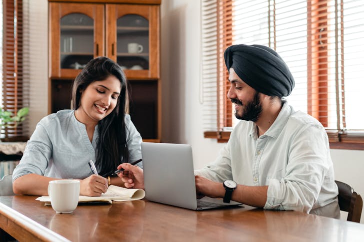 Cheerful young Indian coworkers with laptop discussing project in office