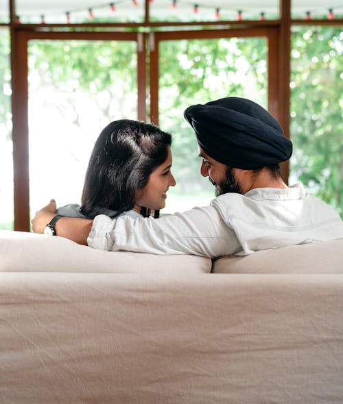 Free Back view of happy romantic young Indian couple cuddling while relaxing on coach in cozy apartment and looking at each other Stock Photo