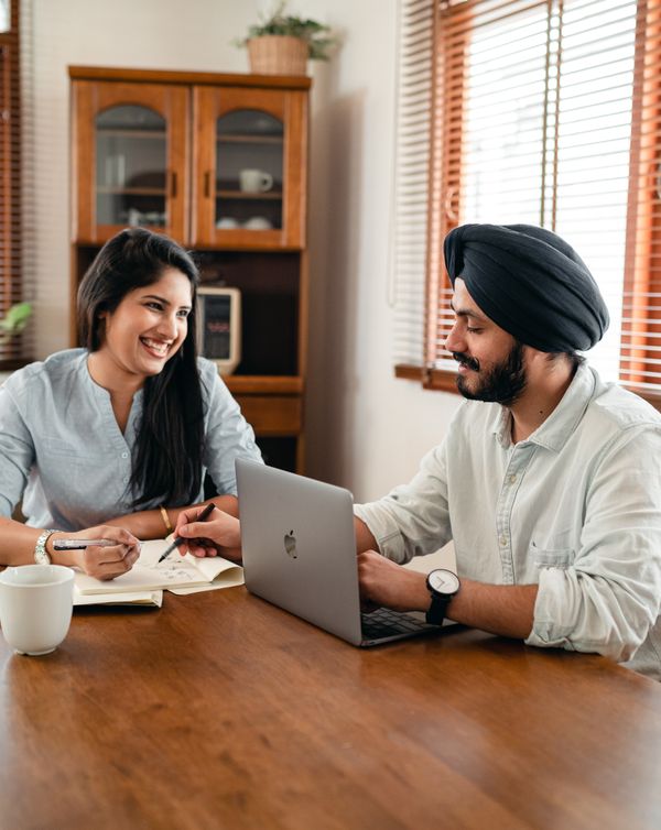 Positive young colleagues working remotely sitting at table with laptop and documents