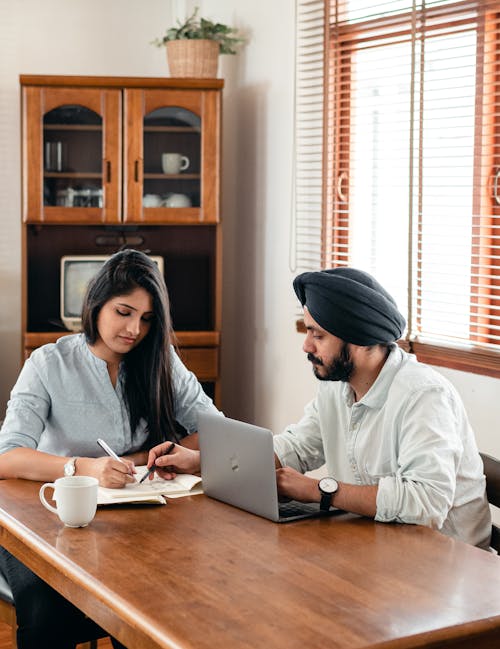 Free From above of young Indian male tutor and female student sitting at table with laptop and exercise books and doing homework during individual lesson Stock Photo