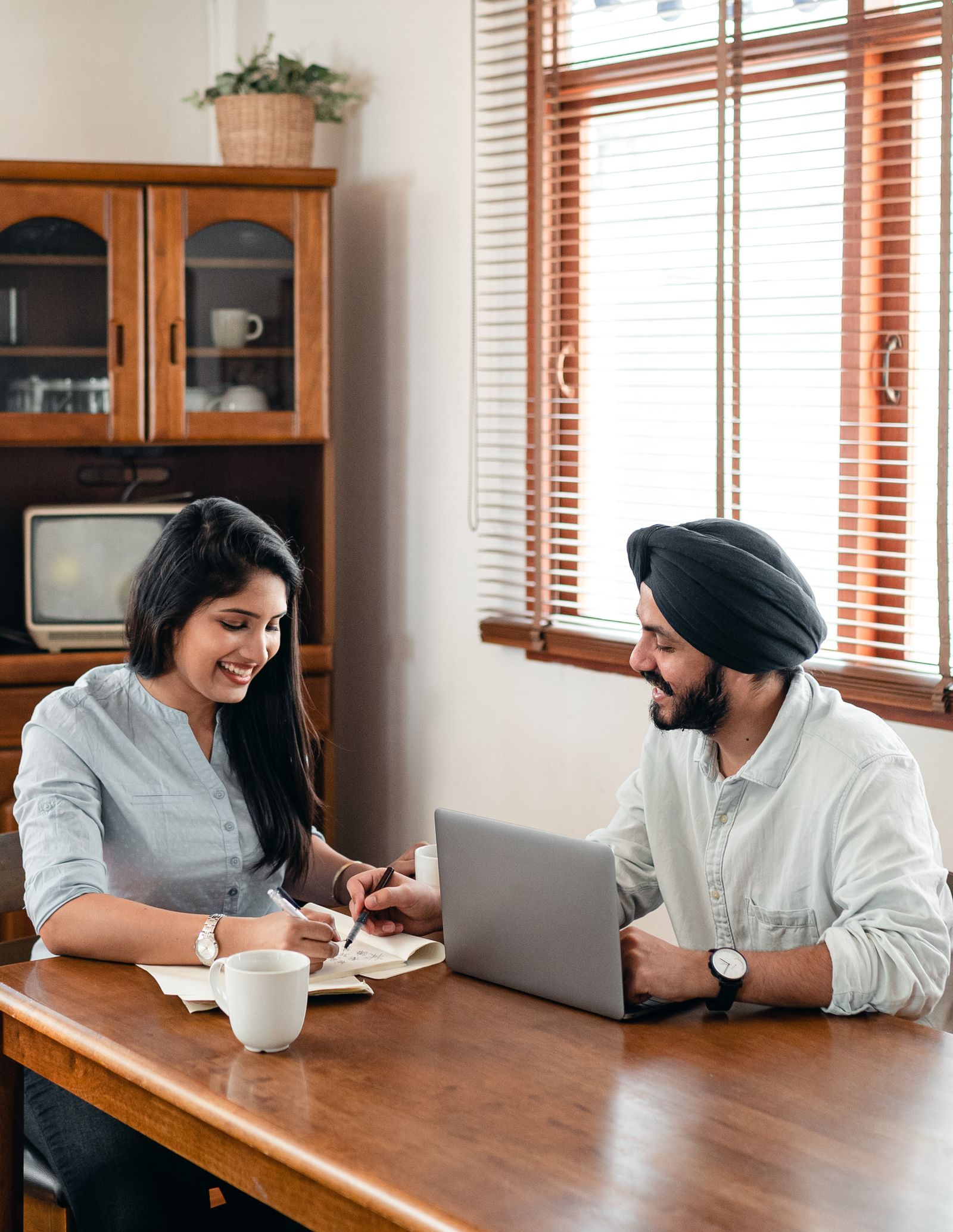 Two young Indian students in casual clothes discussing an assignment together at a bright table with a laptop