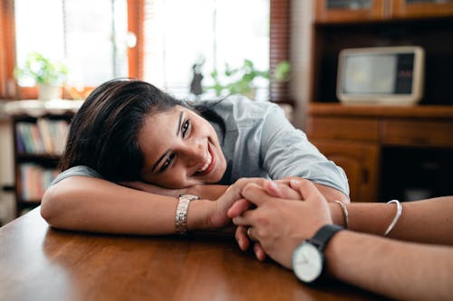 Happy ethnic woman sitting at table and smiling while holding hand of husband