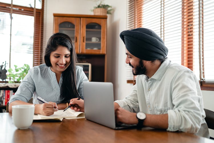 Happy Indian Colleagues Speaking While Surfing Internet On Laptop