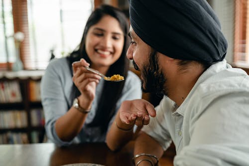 Positive girlfriend feeding crop Indian boyfriend with delicious food