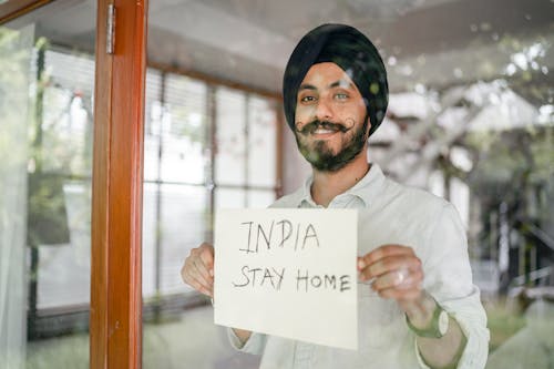 Indian man showing INDIA STAY HOME inscription through glass