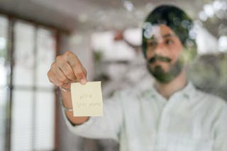 Indian man showing paper sheet while standing behind glass wall