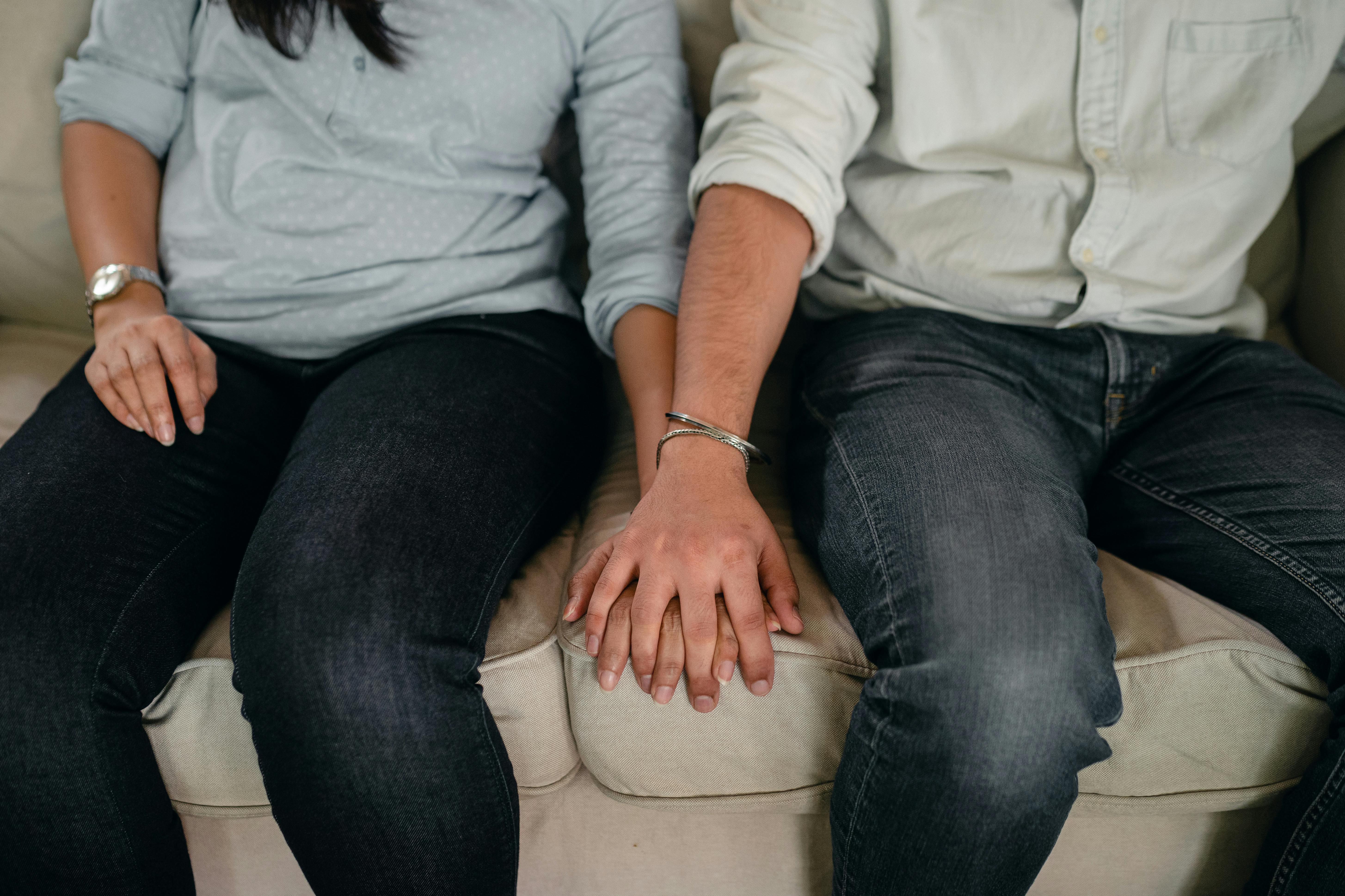 crop couple holding hands on coach