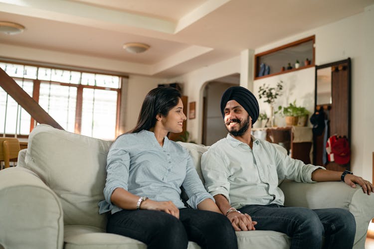 Smiling Young Indian Couple Holding Hands On Couch