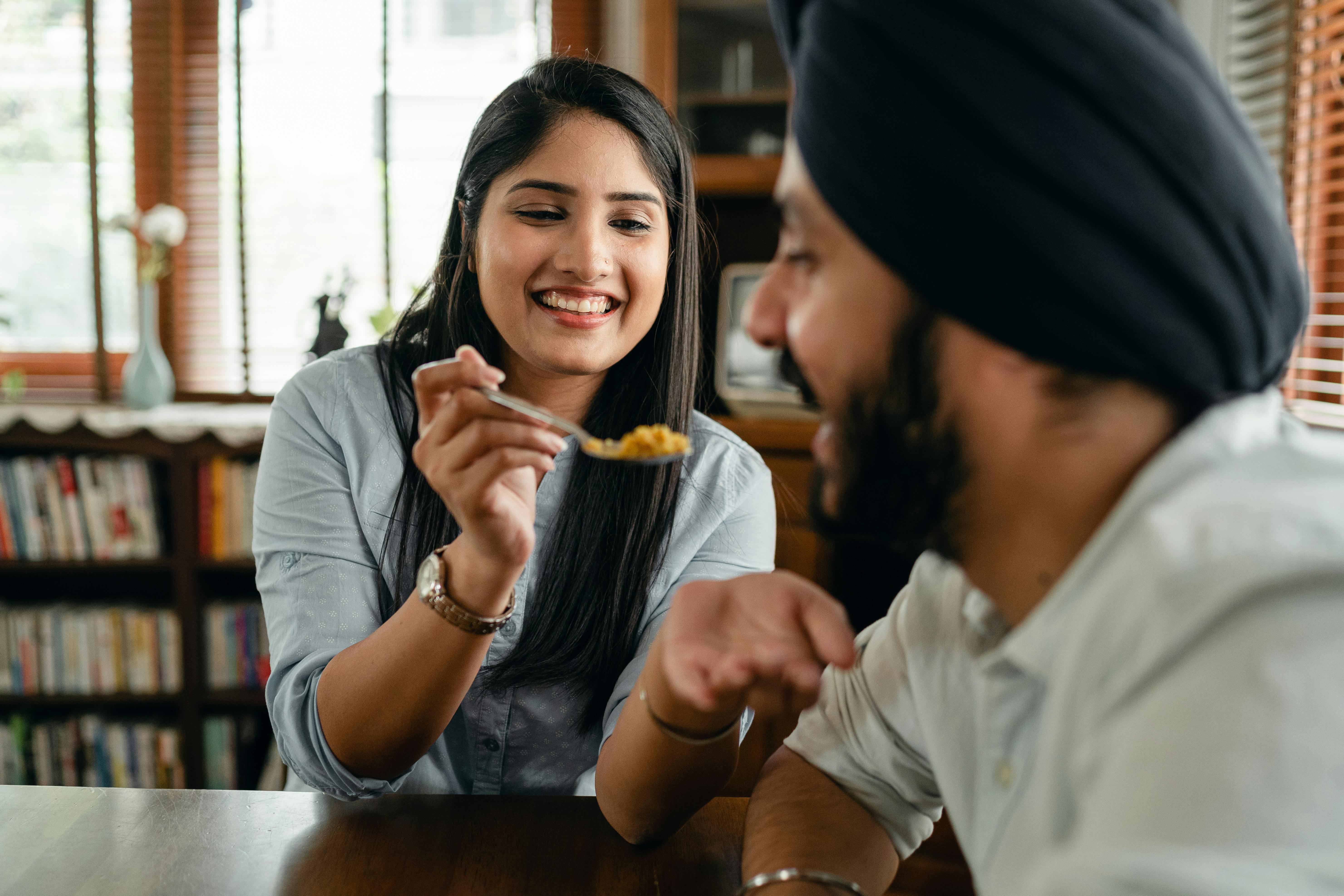 A cheerful young couple shares a joyful moment feeding each other indoors.