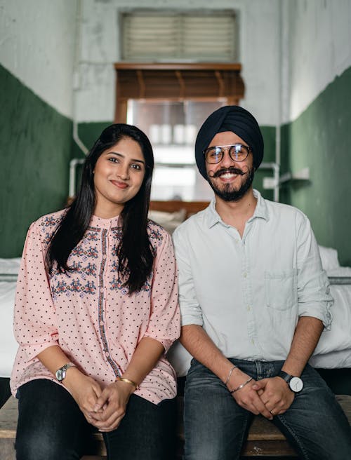 Cheerful young Indian couple smiling while sitting on bench in small room