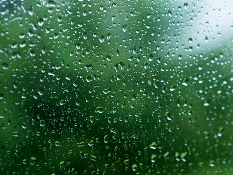 雨滴在玻璃上的特写镜头，与充满活力的绿色背景形成对比，营造出清新而平静的氛围