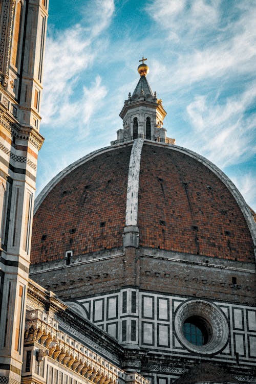 From below medieval church with weathered dome with golden cross located against cloudy sky on sunny day