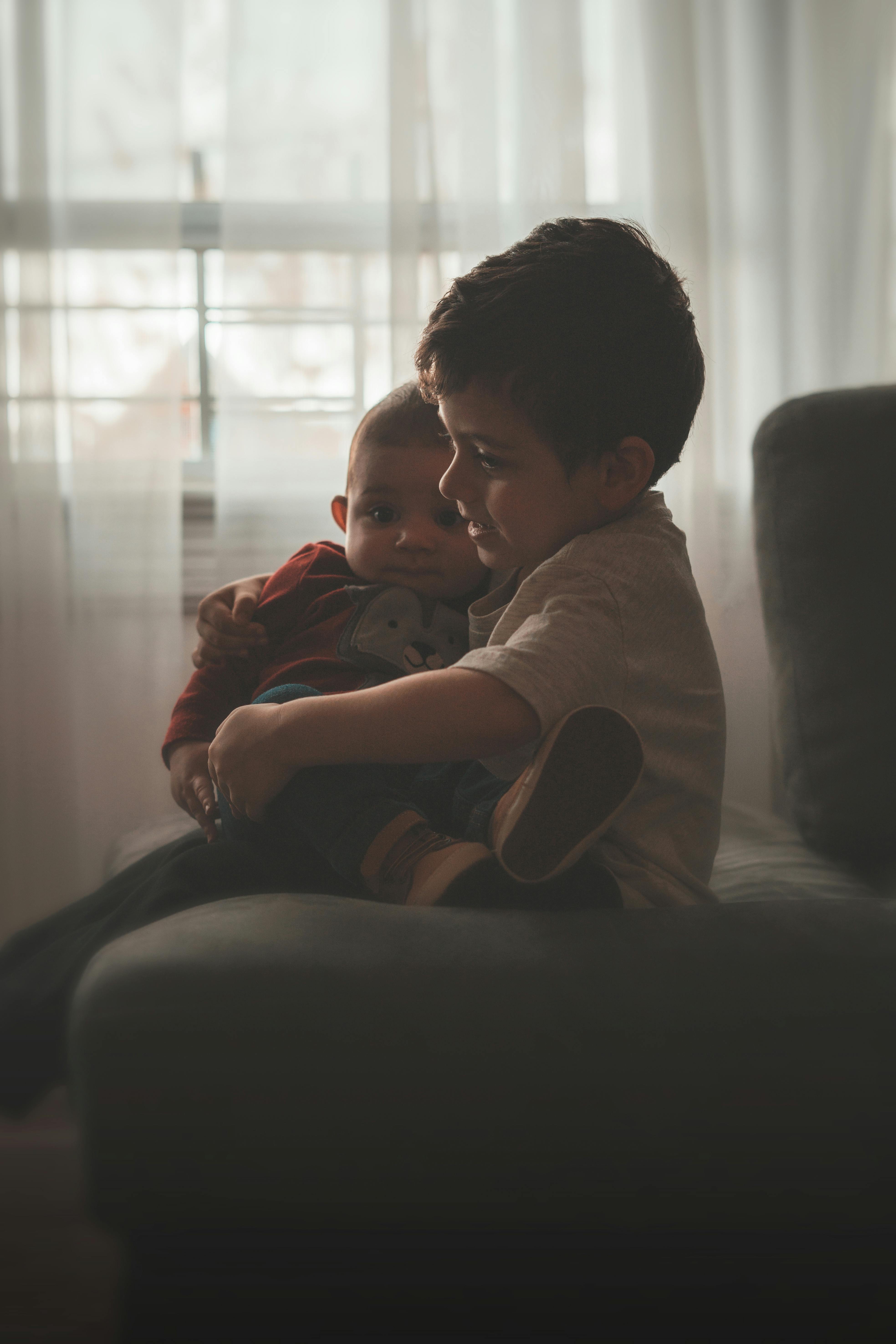一个小男孩在室内的沙发上，深情地抱着他的弟弟妹妹，场景温馨而亲密