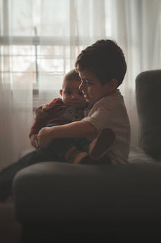 一个小男孩在室内的沙发上，深情地抱着他的弟弟妹妹，场景温馨而亲密