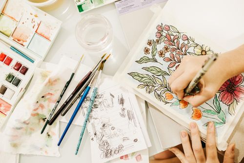 Free Top view of anonymous person painting colorful flowers with watercolor in sketchbook on table in studio Stock Photo