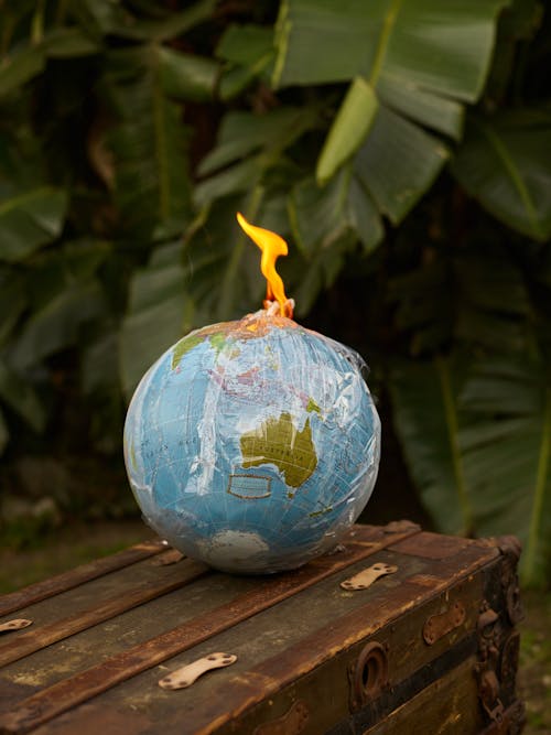 Environment ecology pollution concept burning Earth globe covered in transparent plastic bag in shape of bomb placed on wooden bench near green plants