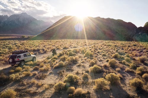 From above picturesque view of highland semidesert area in evening sun with jeep and bike driving on rural road towards hills