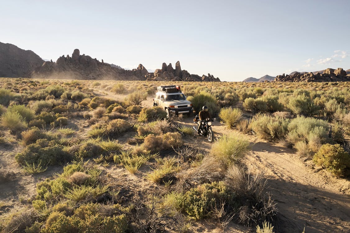 From above scenic landscape of vast dry savanna valley with jeep and bike driving on narrow road in daytime