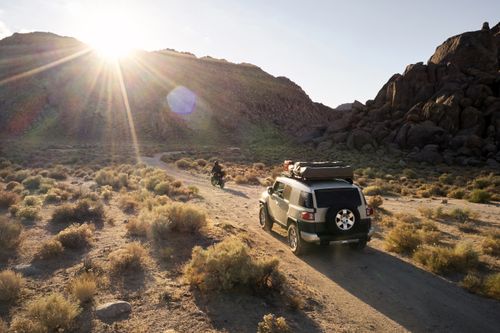 Free Breathtaking landscape with rocky hills and dry vegetation against sundown and car with motorbike on narrow dusty road Stock Photo