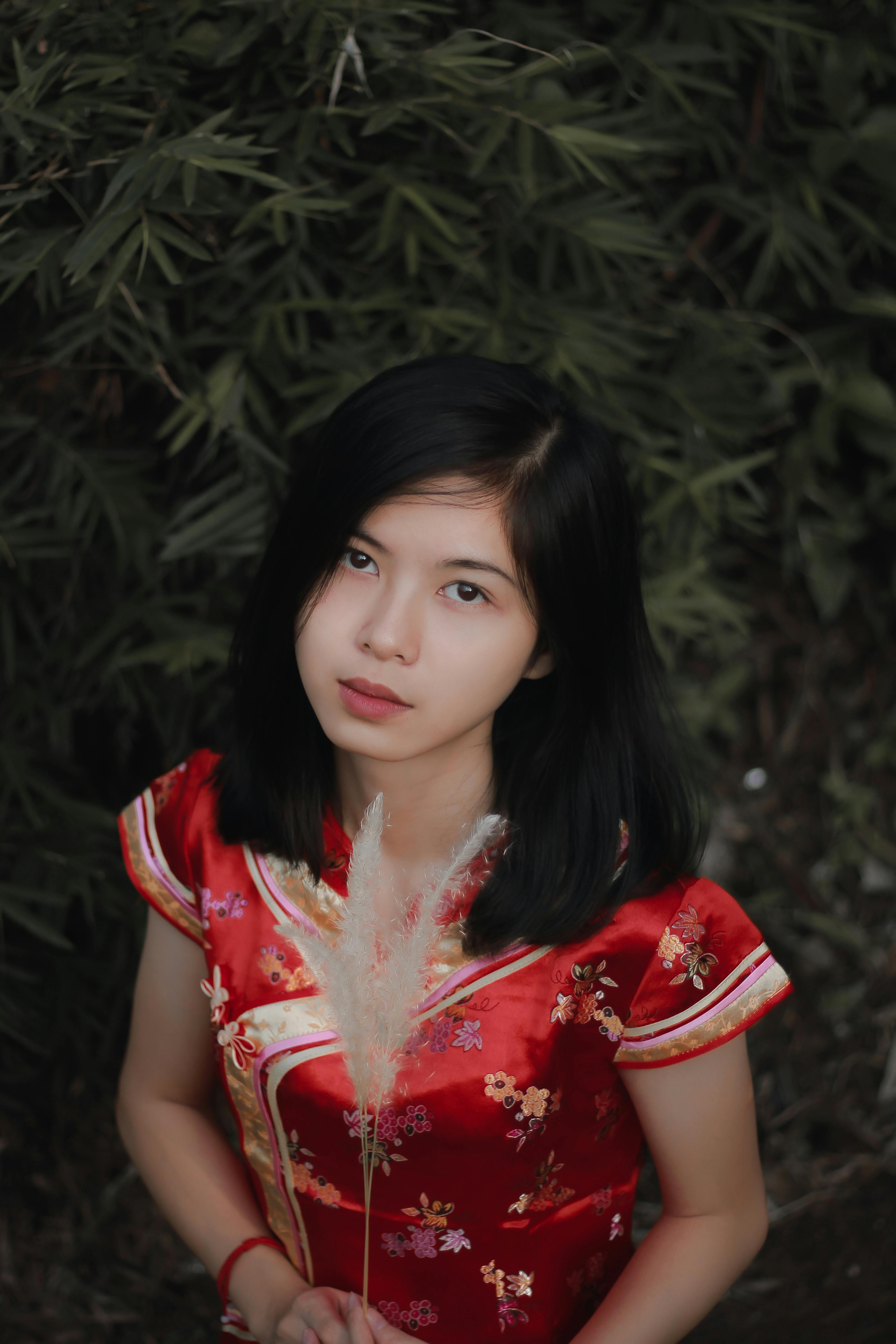 一位年轻女子身着红色传统连衣裙，在户外举着羽毛，四周绿植环绕