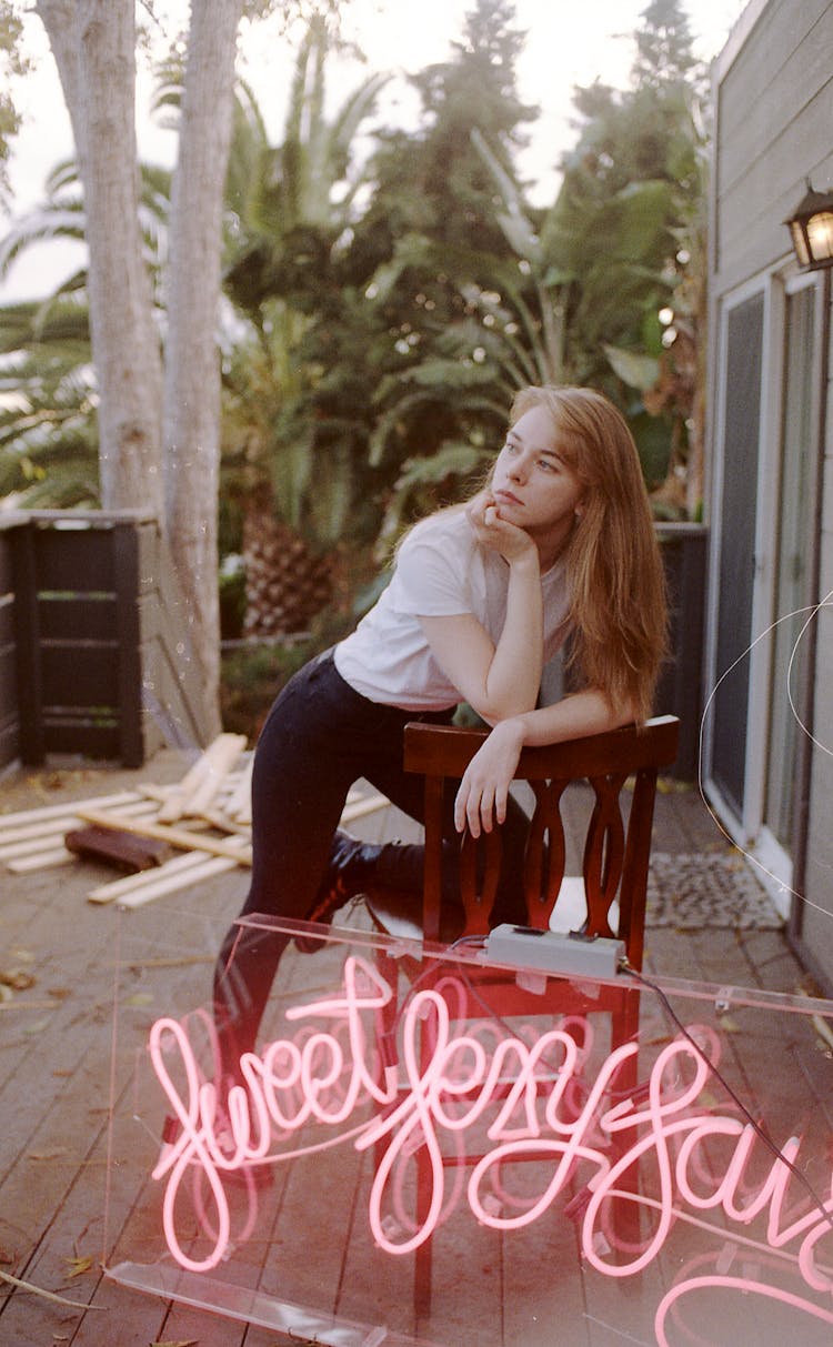 Young Pensive Woman Resting On Porch Near Neon Sign