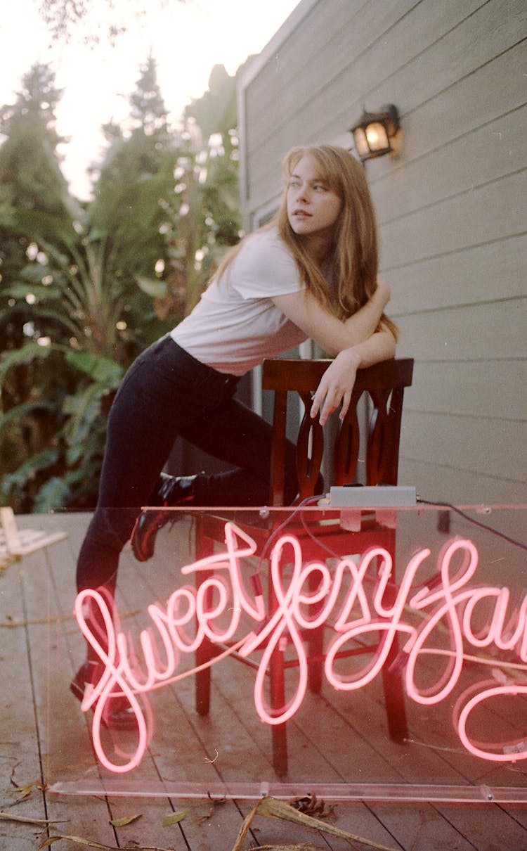 Young Slim Woman Relaxing On Porch Near Neon Decoration