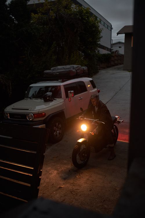 Free From above of unrecognizable brutal male in leather jacket sitting on motorcycle near SUV car at twilight Stock Photo