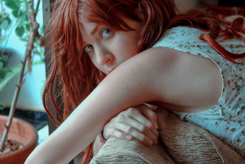 Close-up portrait of a woman with red hair resting indoors, exuding a serene and contemplative mood.