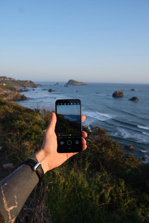 Crop man taking shot of amazing seascape on smartphone from high cliff ...