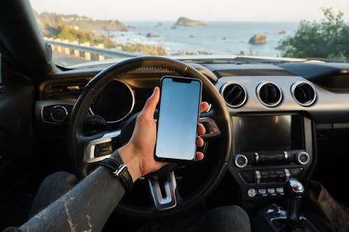 Crop anonymous guy with tattoo on hand navigating on mobile phone while driving car near sea