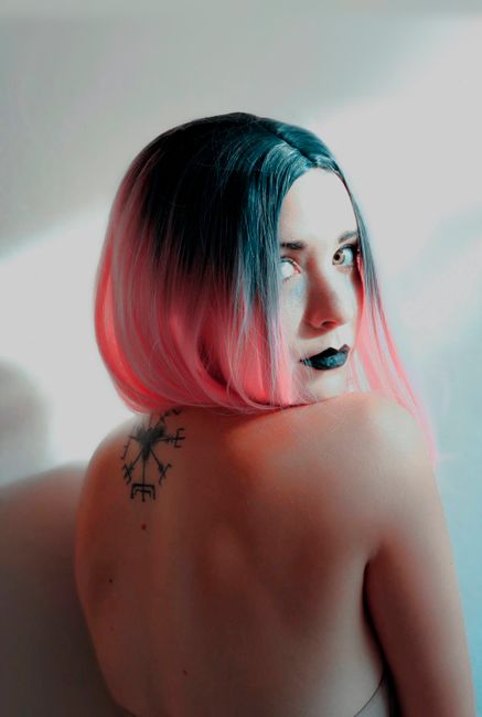 Portrait of a woman with ombre hair and tattoo, highlighting uniqueness and style against a neutral backdrop.