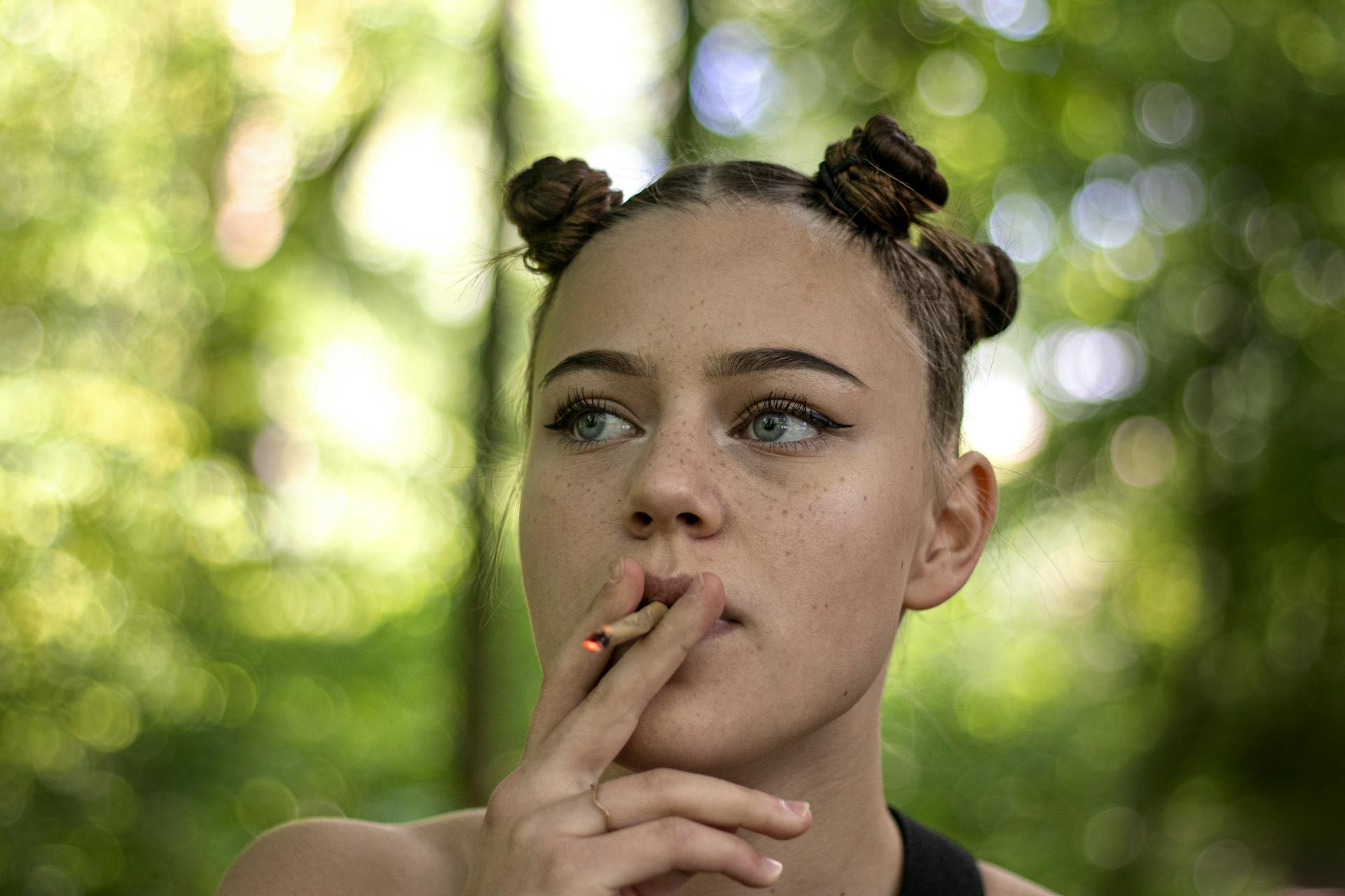 A young woman with a unique hairstyle smokes in a serene outdoor setting.