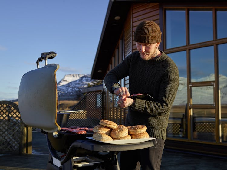 Focused Young Man Grilling Meat On Veranda Of Winter House