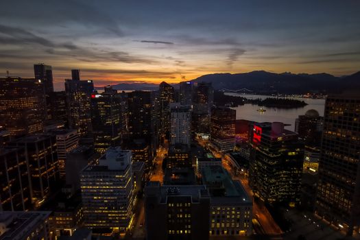 From above of contemporary illuminated city with high buildings located near river and hills