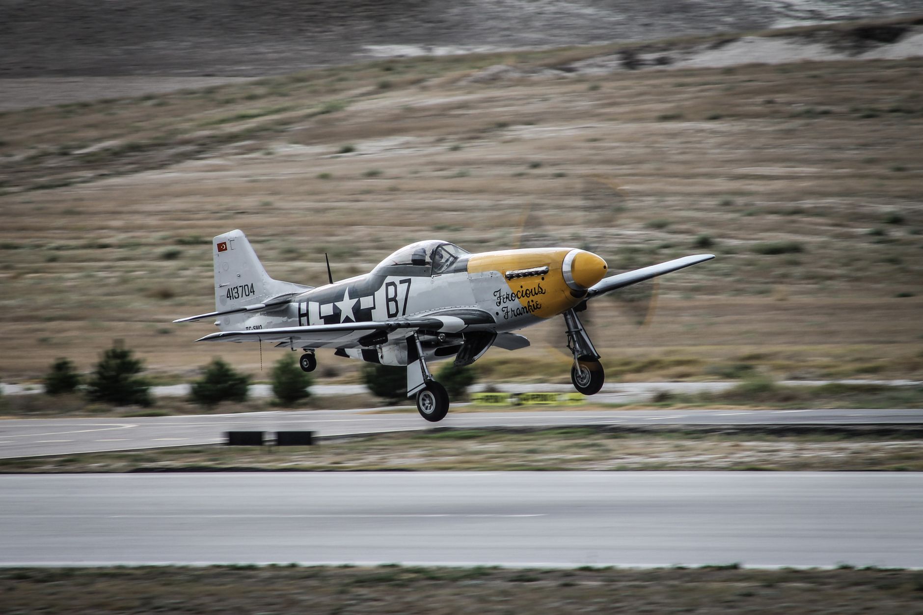 A historic P-51 Mustang fighter plane landing on a runway in Eskişehir, Türkiye.
