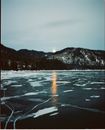 Winter scenery with snowy mountains and frozen lake with sun reflection on sunset