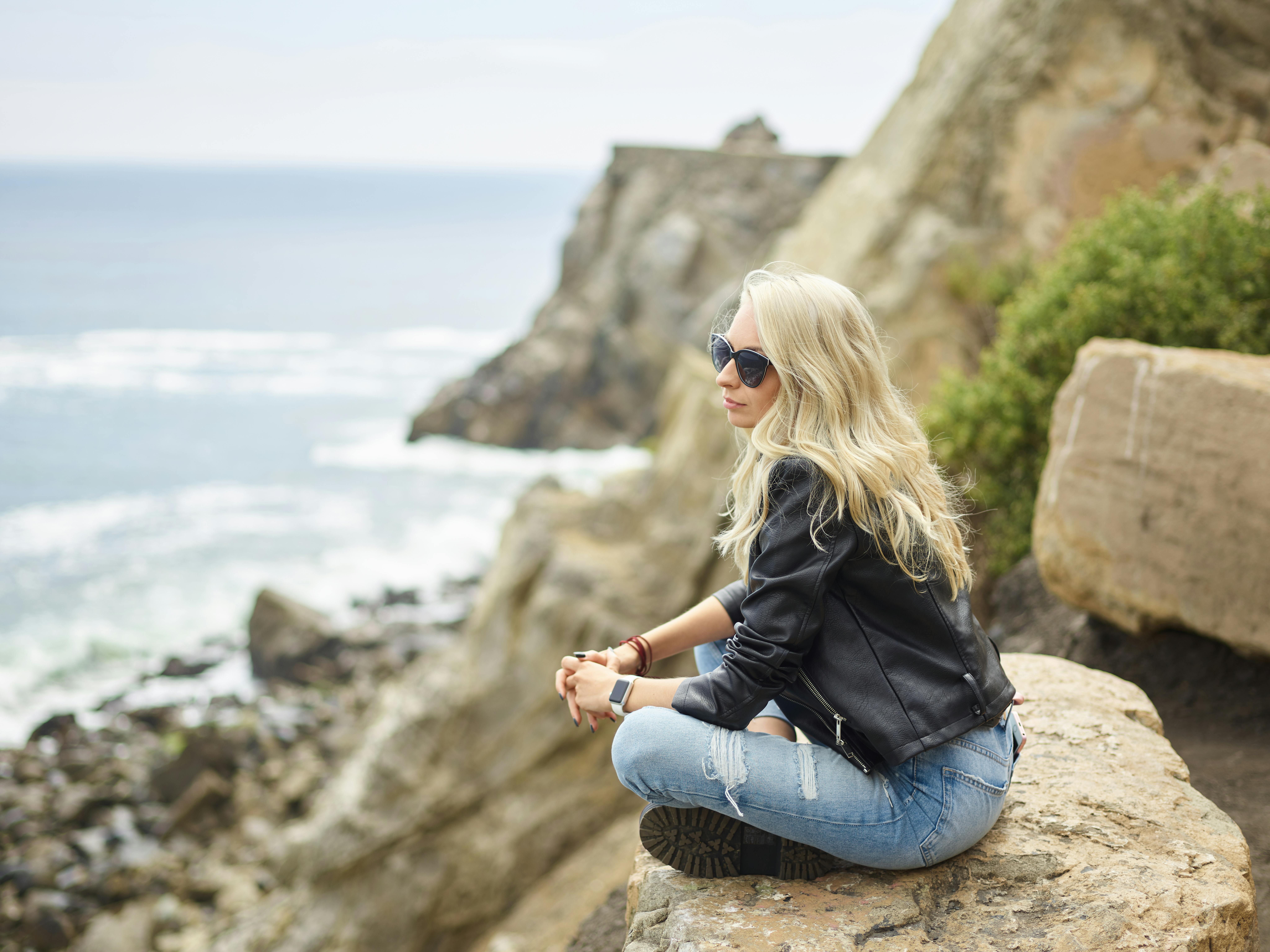 Calm stylish woman enjoying view of ocean sitting on cliff · Free Stock