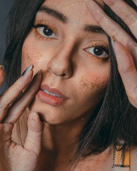 Crop young calm woman with glowing bright makeup with glitter looking at camera