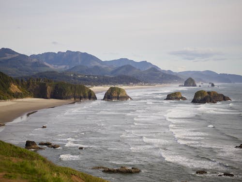 Picturesque view of rocky coastline of ocean against mountain ridges and sky during sunset