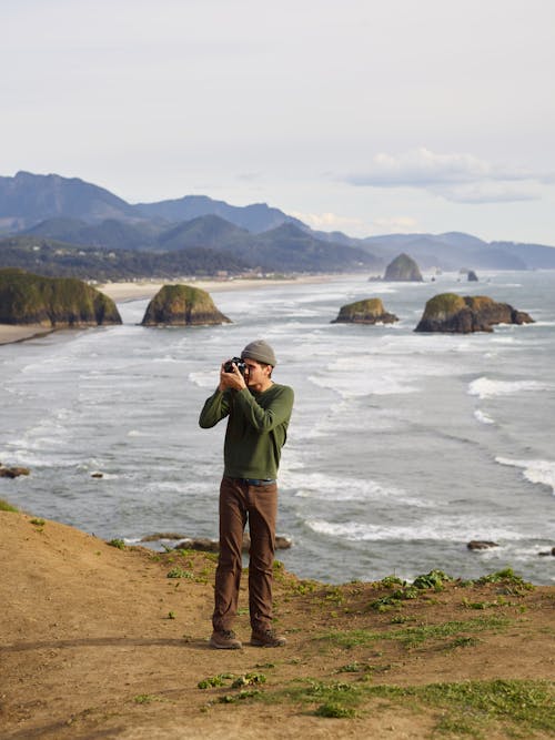 Free High angle of young male photographer in casual clothes standing on rocky viewpoint and taking pictures of amazing landscape with camera Stock Photo