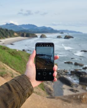 Crop unrecognizable tourist capturing beauty of rocky shoreline and magnificent sea on modern smartphone on fine day